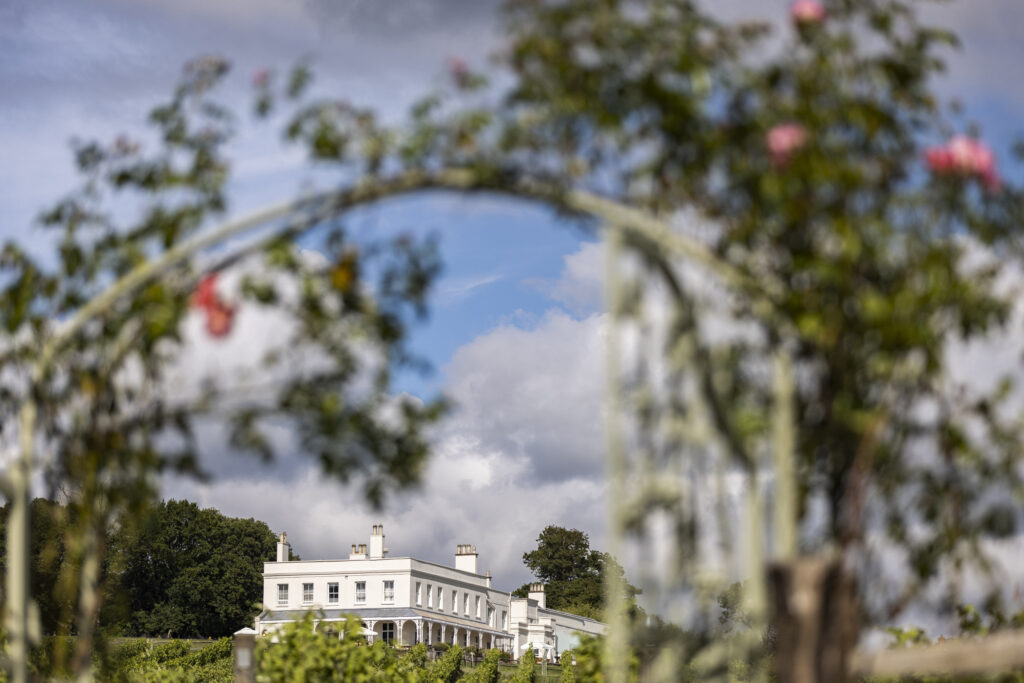 Lympstone Manor Hotel and Vineyard viewed through a rose arch from the bottom of the vineyard
